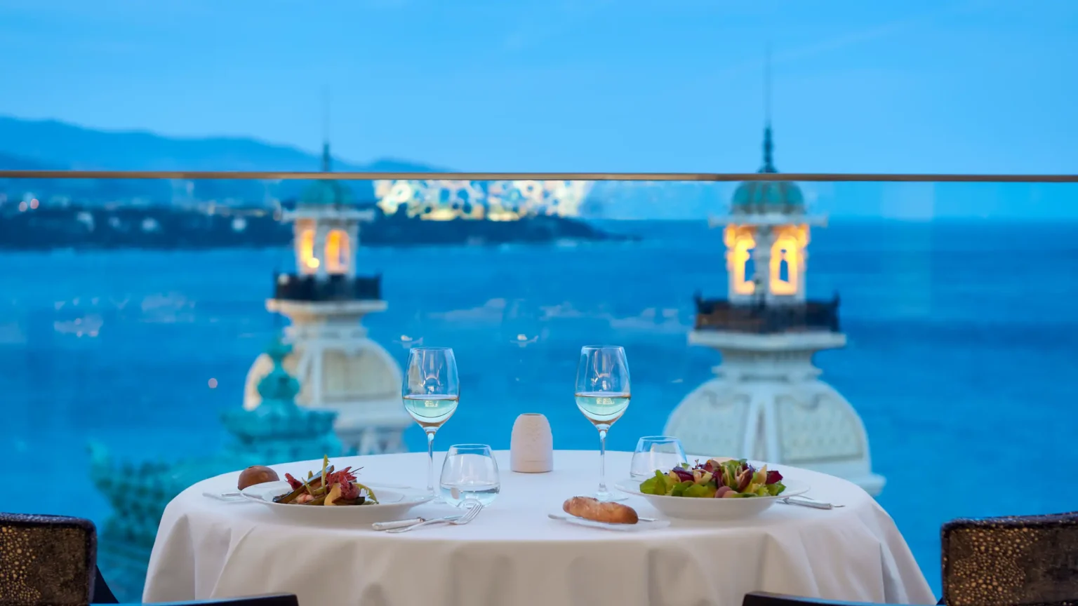 stół z białym obrusem, dwoma kieliszkami na tle morza