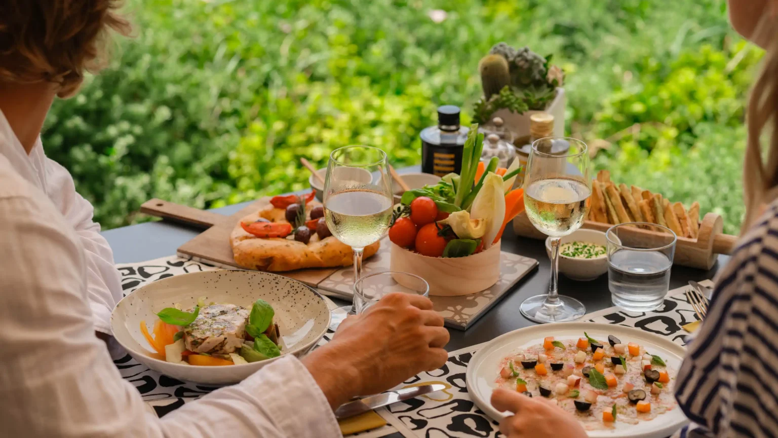 mężczyzna i kobieta siedzący przy stole z zastawionym stołem jedzeniem na tle przyrody