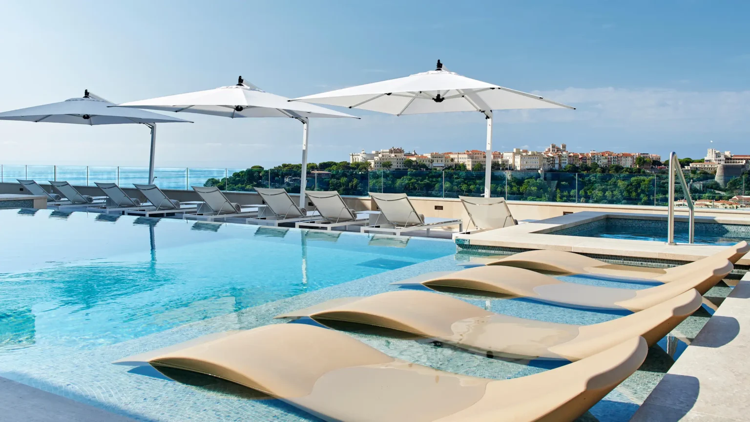 basen hotelowy z leżakami opadającymi do wody i białymi parasolami