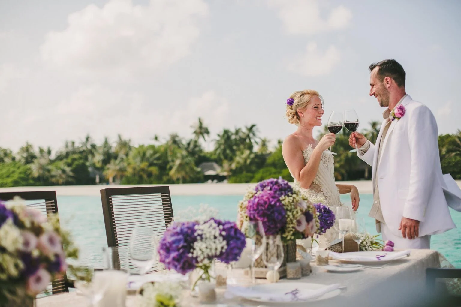 a woman and a man dressed in white clothes holding drikas in their hands against the background of the sea and palm trees