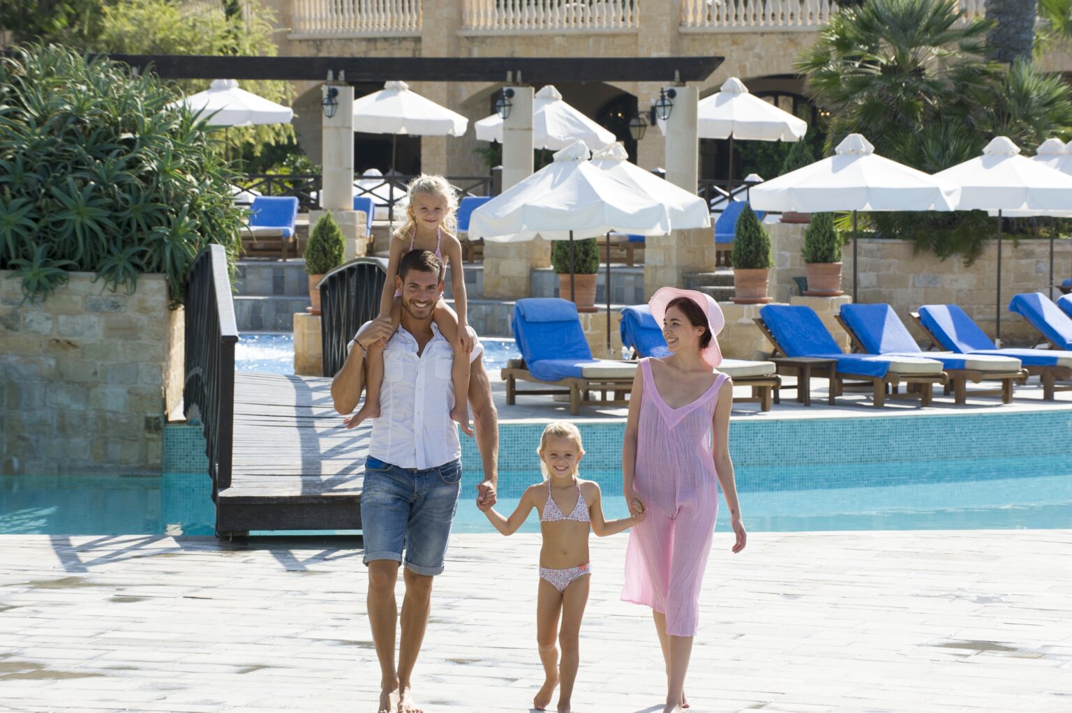 rodzina mama tata i dwojka dzieci spędzająca czas nad basenem i spacerująca po podwórzu hotelu Elysium Hotel