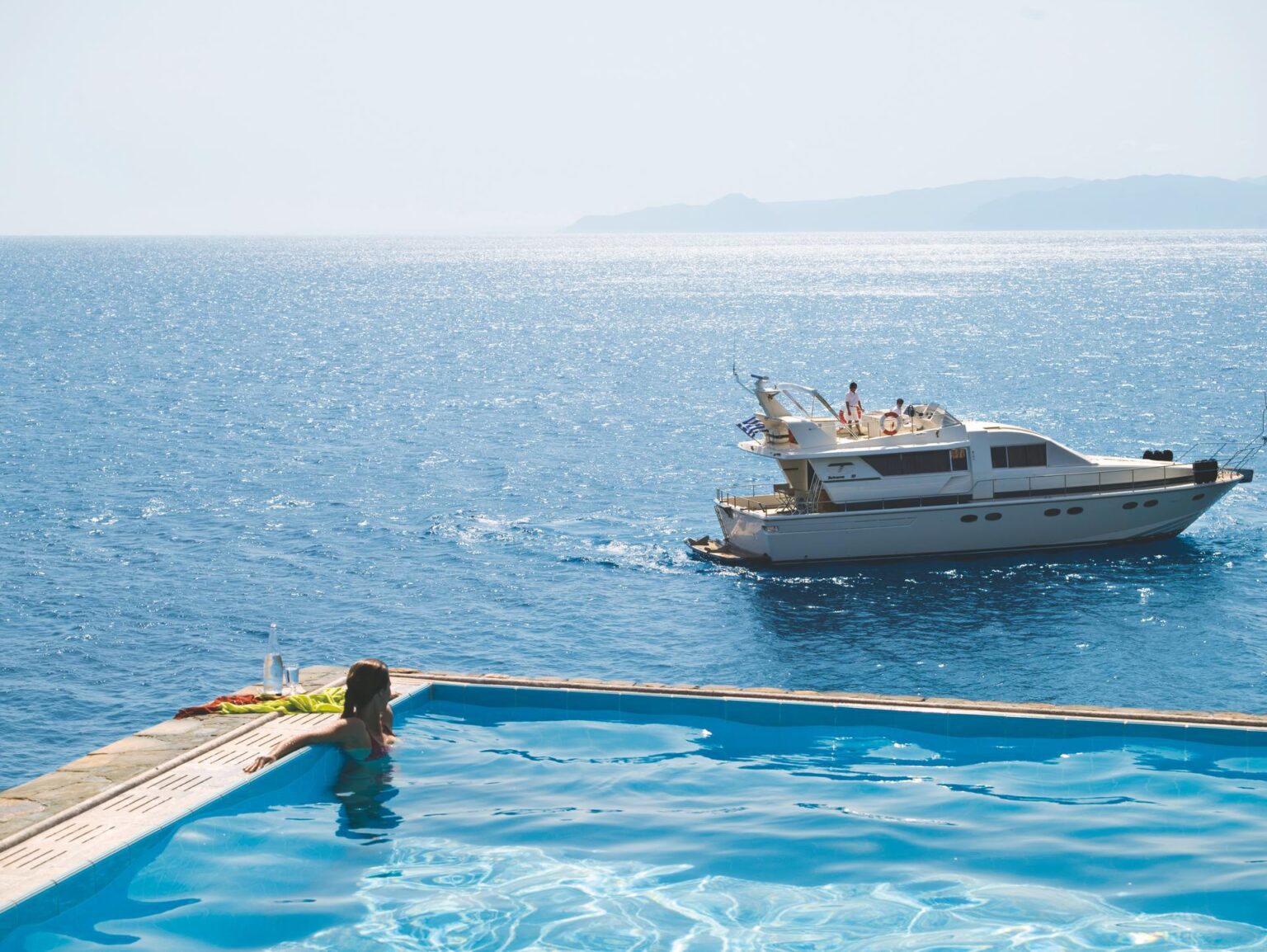 Elounda Peninsula Luxury Resort kobieta obserwująca z basenu bez krawędzi statek w tle na morzu