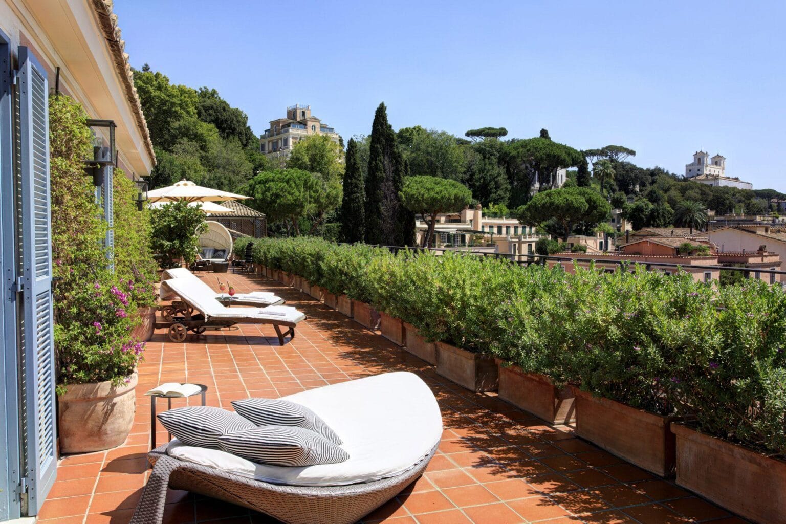 The balcony of Rocco Forte Hotel De Russie with wooden chairs and a table with food and wine