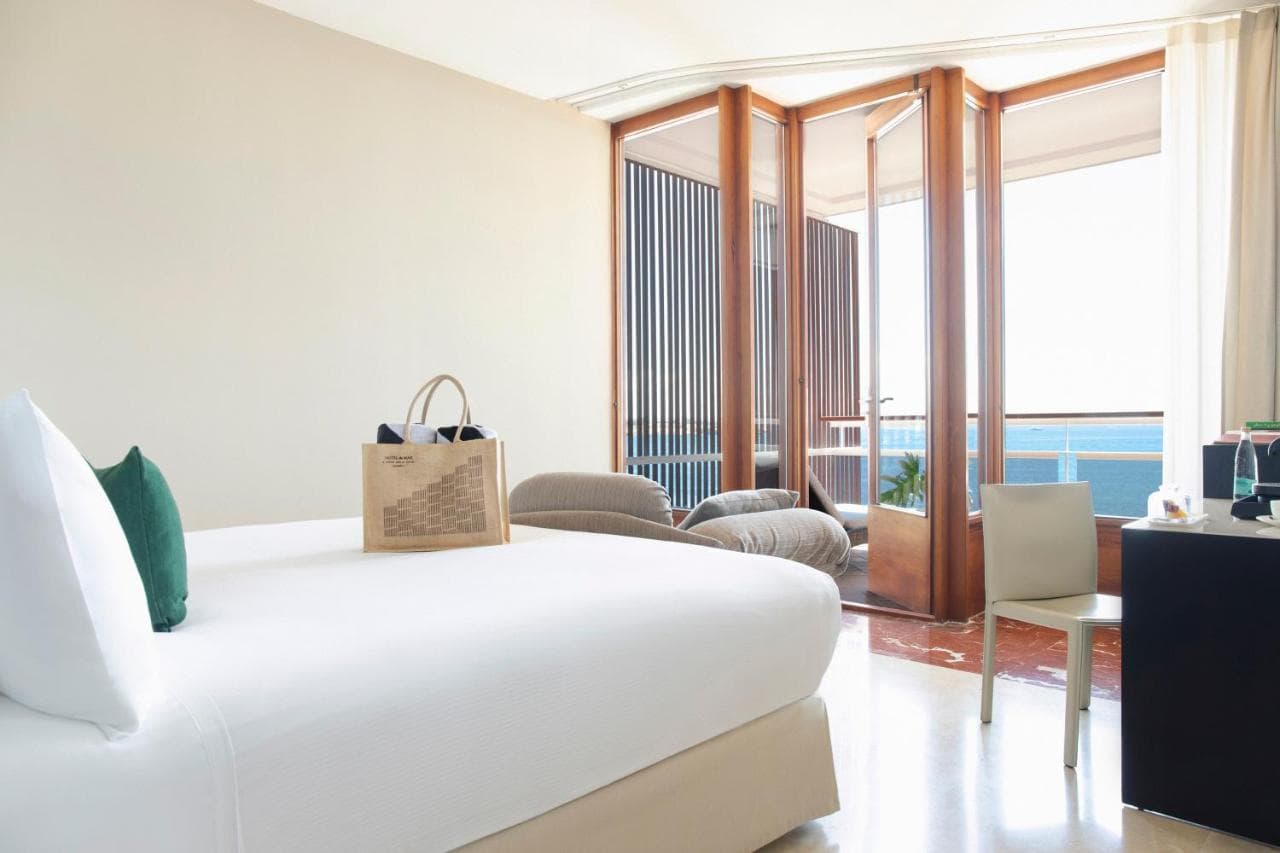 jasna sypialnia z białym łózkiem, na którym leży torba w kolorze beżowym