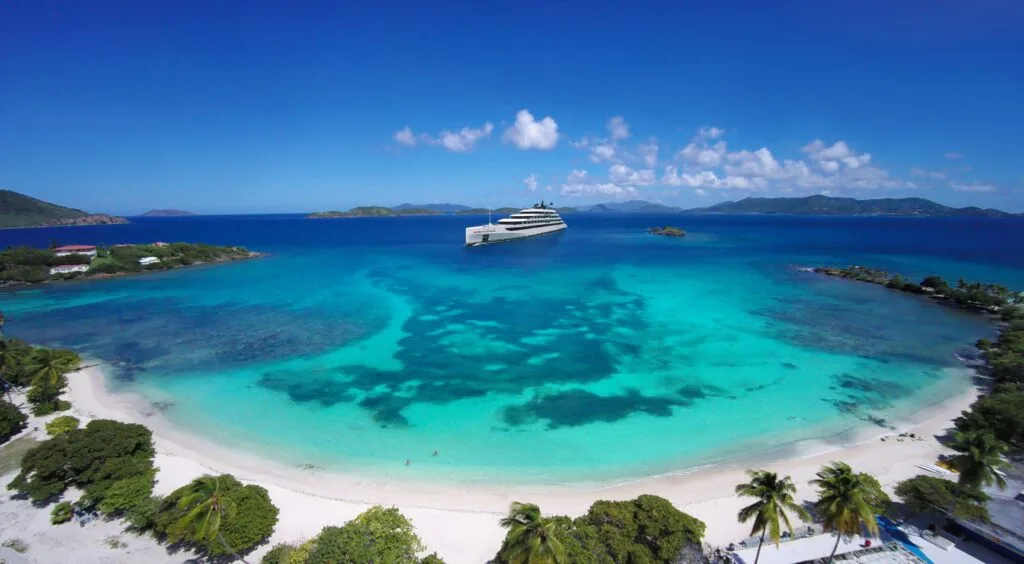 Zdjęcie przedstawia egzotyczną plażę w otoczeniu palm. W tle znajduje się wycieczkowiec Emerald Cruises