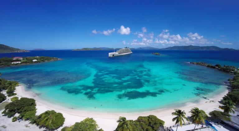 Zdjęcie przedstawia egzotyczną plażę w otoczeniu palm. W tle znajduje się wycieczkowiec Emerald Cruises