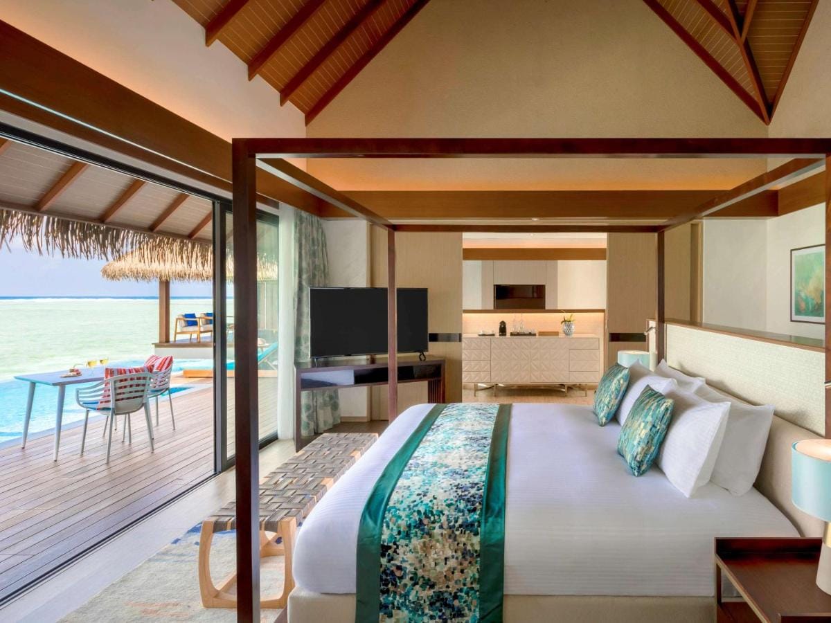 pullman maldives all inclusive resort przykładowa sypialnia z widokiem na otaczającą roślinność i ocean, wyoskie sklepienie dachu w brązowym kolorze, jasna i przestronna sypialnia