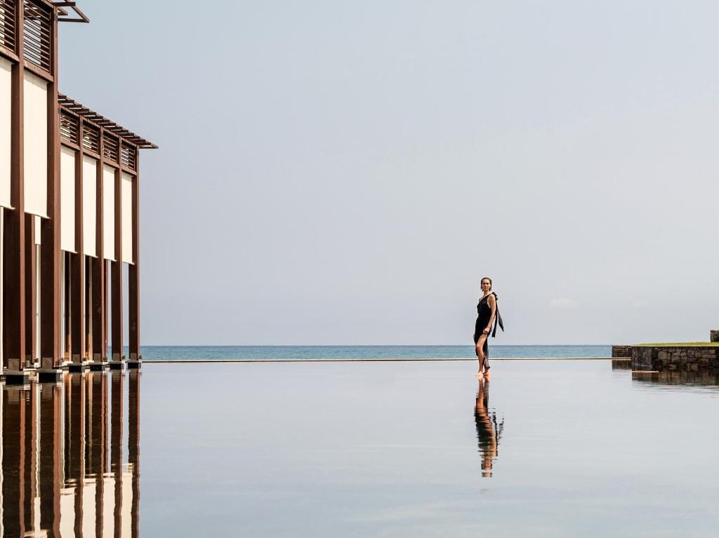 amirandes a grecotel resort to live kobieta stojąca na brzegu basenu z widokiem na morze