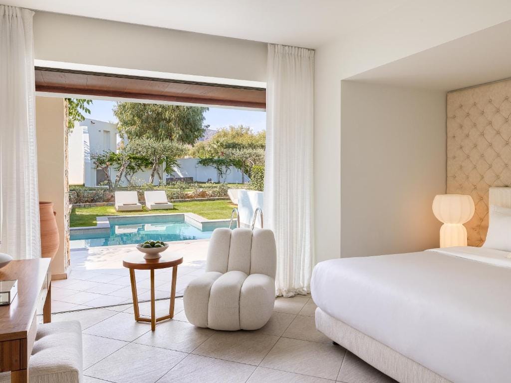 amirandes a grecotel resort to live jasny i elegancko urządzony pokój - łóżko i fotel z widokiem na taras z basenem