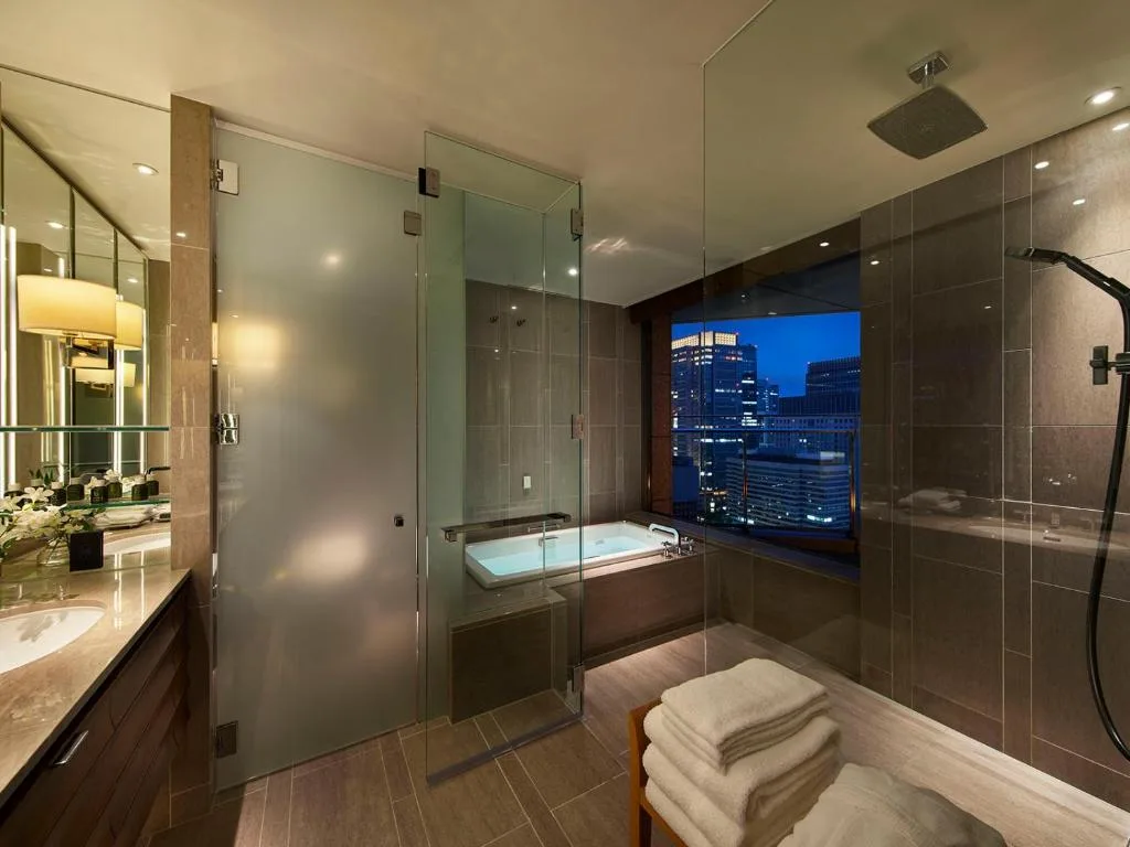Светлая ванная комната в отеле Palace Hotel Tokyo с ванной с подсветкой и видом на город.